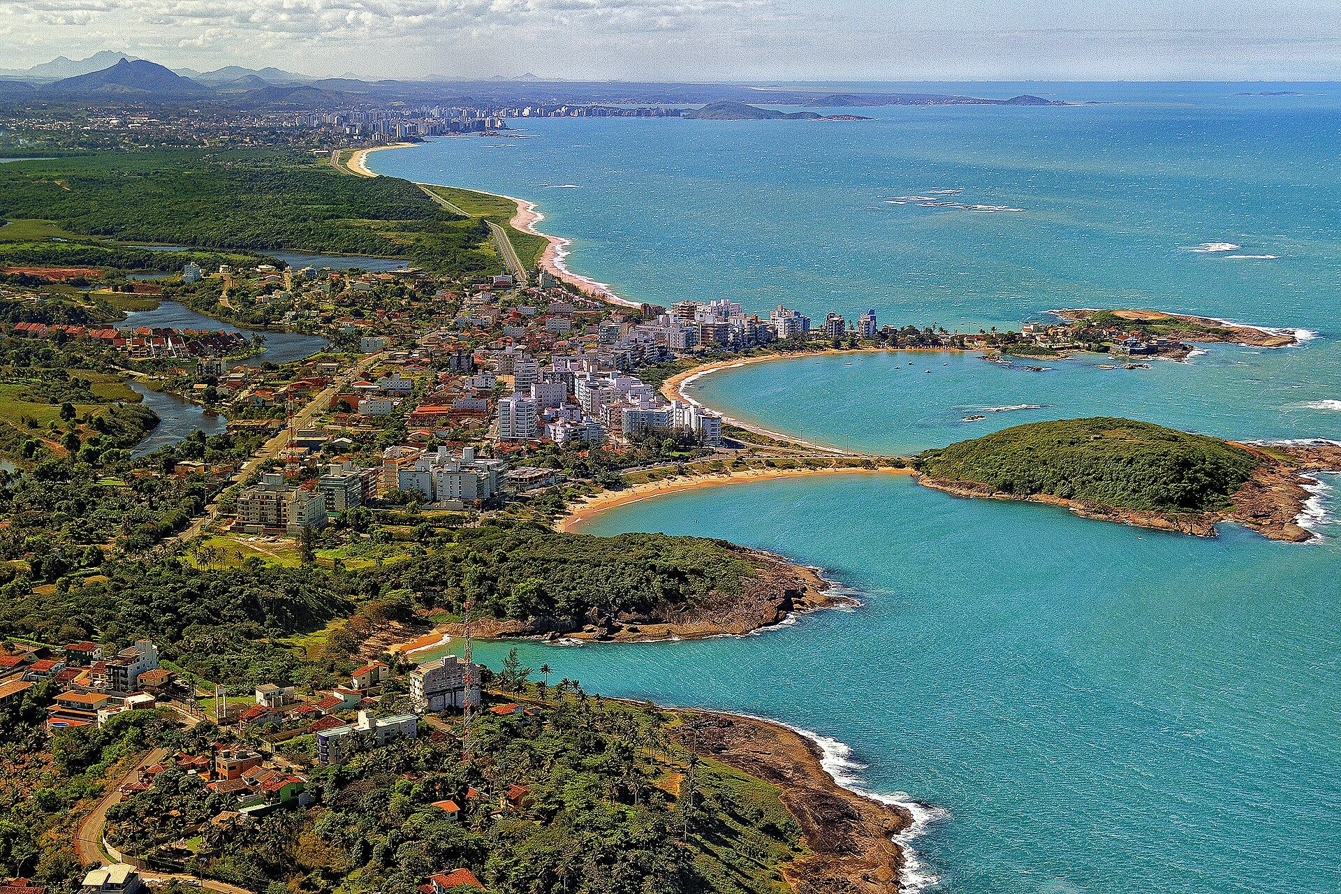 Enseada Azul em Guarapari, com água calma, faixa de areia curva e vegetação costeira.