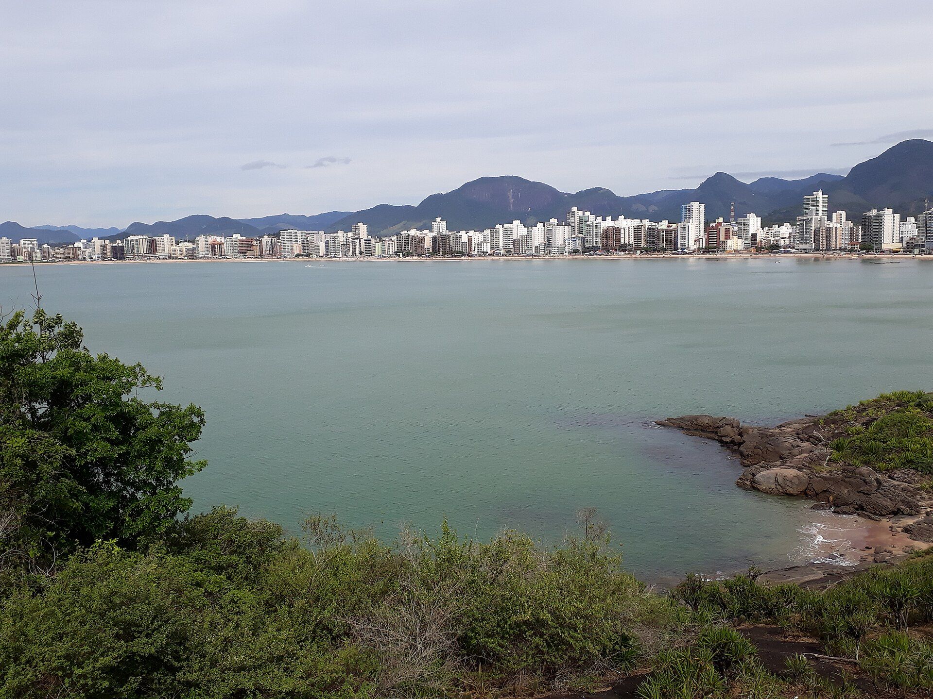 Relevo verde e horizonte costeiro do município de Guarapari vistos do alto.